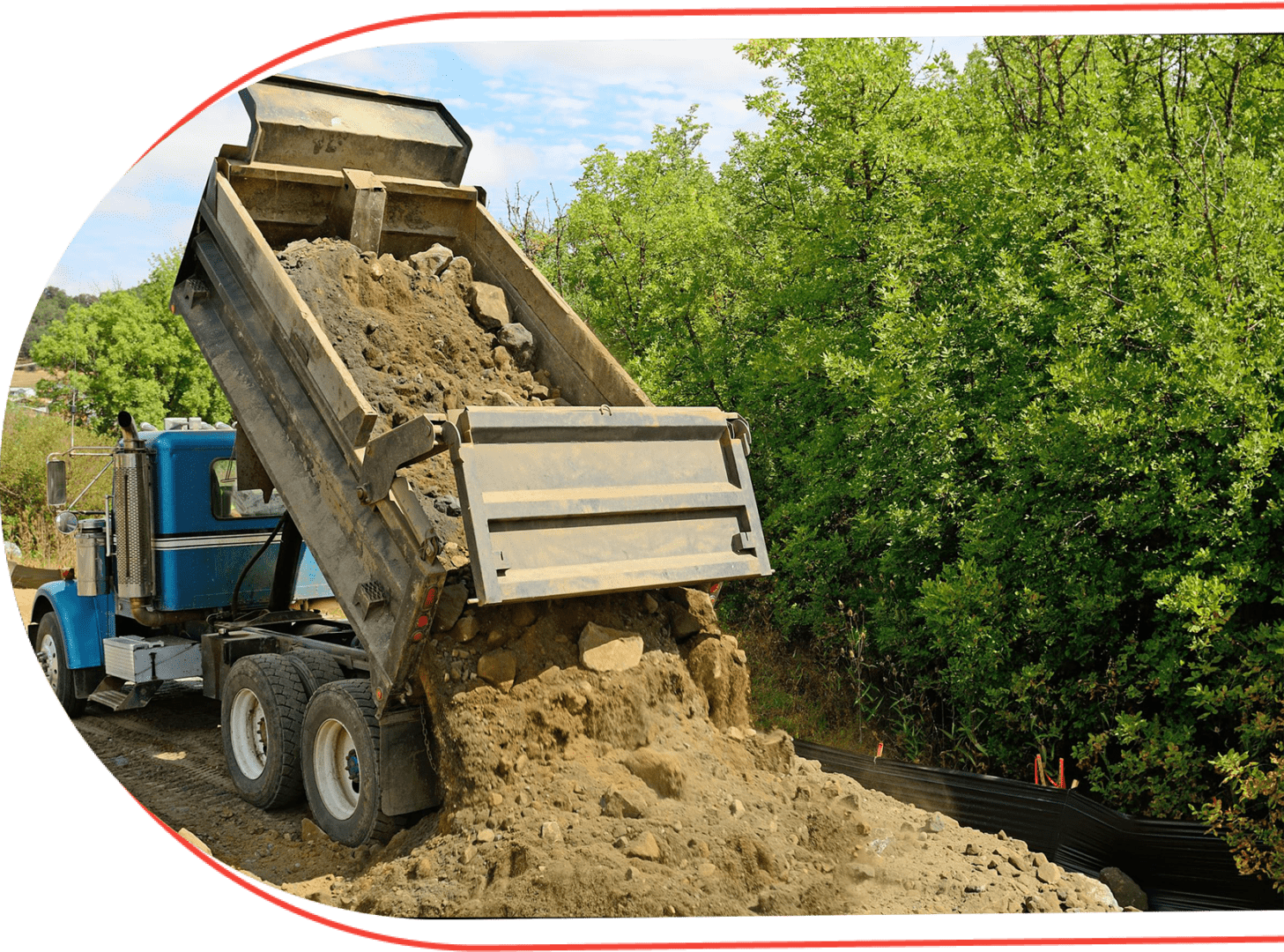 A dump truck dumping dirt on the side of a road.